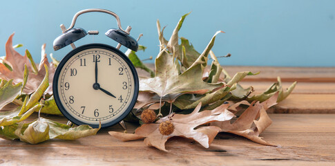 Fall Back Daylight Saving Time. Black clock and autumn leaves on wood