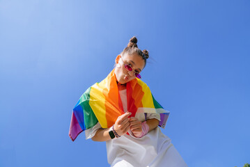 A young woman develops a rainbow flag against the sky