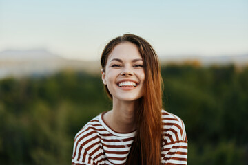 A young woman in a striped T-shirt sincerely laughs with her mouth open while traveling against the backdrop of autumn nature