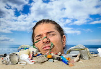 Man buried in sand on beach with rubbish