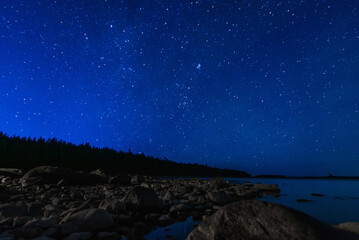 starry sky with constellations, galaxies, milky way and many stars above water of river with stones...