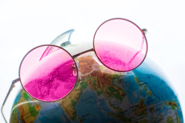 Round glasses with pink lenses on a globe mockup. The concept of world delusion, a distorted view of reality, wearing rose-colored glasses.