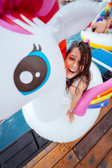 Happy young woman sitting on inflatable unicorn toy mattress