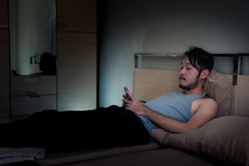 Young man using Mobile Phone on the bed at night.