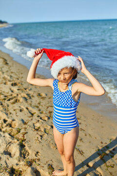 Happy little gorl in christmas Santa hat standing at the beach