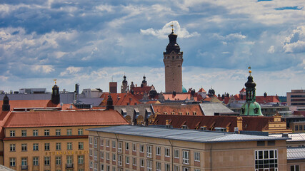 Obraz premium Blick über die Dächer der Innenstadt mit dem markanten Turm des Neuen Rathauses unter dramatischem Wolkenhimmel, Leipzig, Sachsen, Deutschland