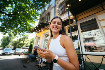 Smiling woman holding phone outdoors in cafe.