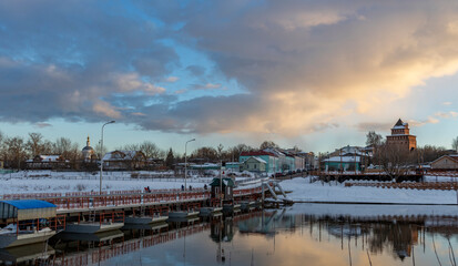 Winter landscape with a river in the old town. Evening, clouds are reflected in the water. Pantone bridge across the river.
