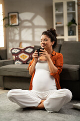 Cheerful pregnant woman holding cup of tea in living room. Beautiful woman enjoy in hot drink..