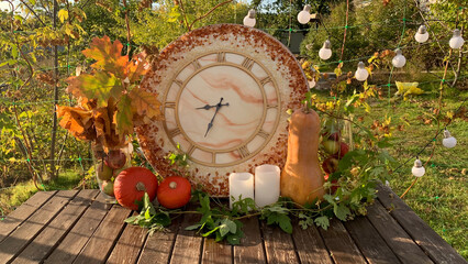 Fototapeta premium Autumn garden home decoration composition with clock, pumkins, candles and apples. Fall yard arrangement on the table or other zone