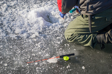 A fisherman breaks ice with an ax on the river to catch fish