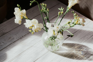 White roses stand in a vase on white wooden boards.