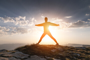 Silhouette of a happy woman at sunset or sunrise, standing with raised hands on top of a mountain...