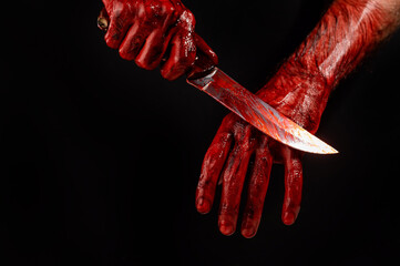 A man wipes a bloody knife with his hand on a black background. 