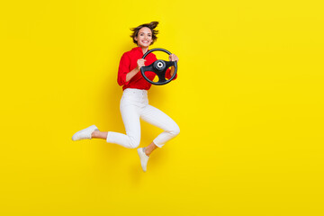 Fototapeta na wymiar Full length photo of overjoyed cheerful person jumping arms hold wheel isolated on yellow color background