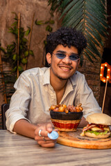 Latin young man with curly hair paying for a typical meal and a hamburger with a bitcoin coin in a restaurant