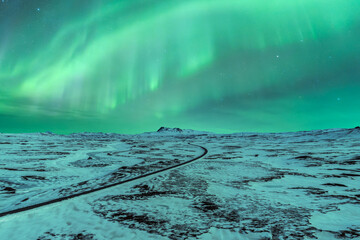 Empty asphalt road amidst field covered with snow under sky with northern lights