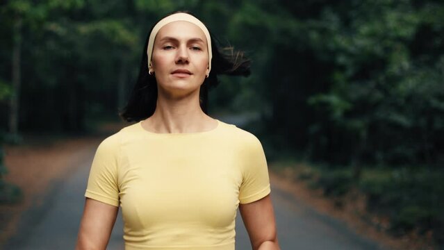Active young adult woman training in the forest. The fitness female is jogging outdoor. Concept of workouts running and healthy lifestyle. Yellow and green.