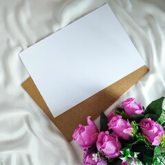 Top view of artificial bouquet and blank paper on the white piece of cloth