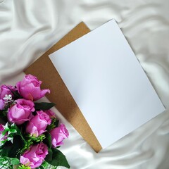 Top view of artificial bouquet and blank paper on the white piece of cloth