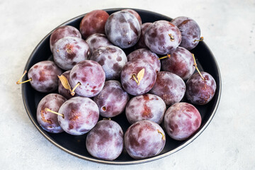 Fresh purple fruit plum on a wooden plate on a light background, top view