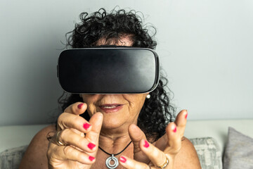 Frontal image of an older, brunette, curly-haired woman wearing virtual reality goggles and using...