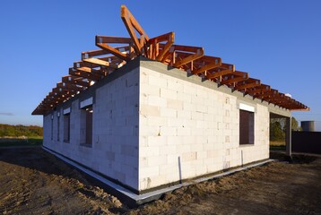 Dom jednorodzinny w budowie w stanie surowym z widoczną drewnianą kontrukcją dachu