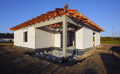 Dom jednorodzinny w budowie w stanie surowym z widoczną drewnianą kontrukcją dachu