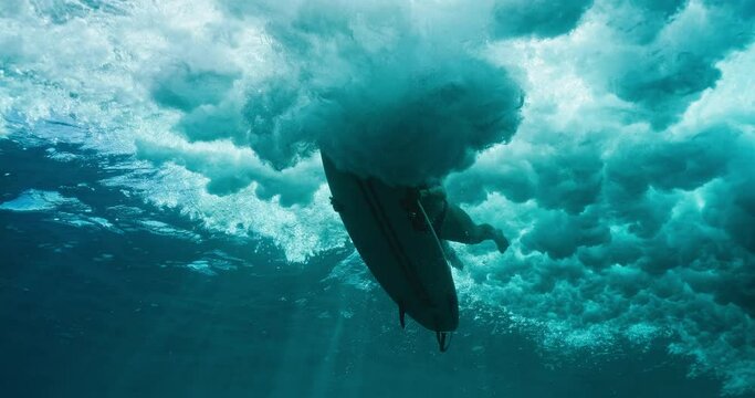 Surfer girl dives under large ocean wave on surfboard, underwater view of woman duck diving