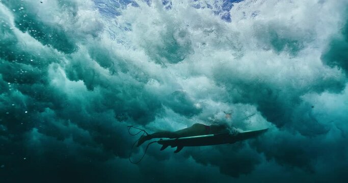 Underwater view of surfer girl diving under ocean wave, duck diving below the surface, slow motion