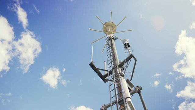 Communication devices and weather measurements equipment on top of tall antenna. Camera moves slowly in low angle showing data transmission gear and instruments in tall tower under blue sky - Powered by Adobe