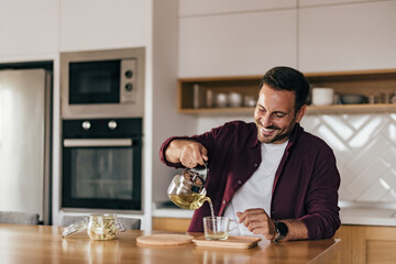 Smiling man pouring tea into a cup, ready to drink it.