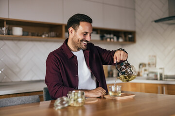 Smiling man pouring tea into a cup, ready to drink it.