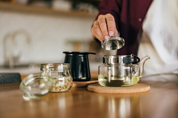 The male person holding a kettle lid just prepared tea in a teapot.