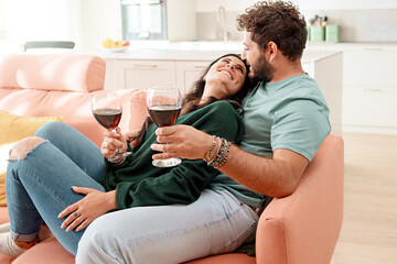 Happy newlywed young couple sitting on the couch and drinking wine for valentines' day at their new apartment