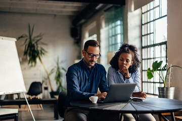 African woman sitting next to her male boss, learning new things about work.