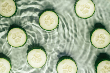 Cucumber slices lie on surface of rippled transparent fresh green water gel with fleck, waves, shadow, expanding circles