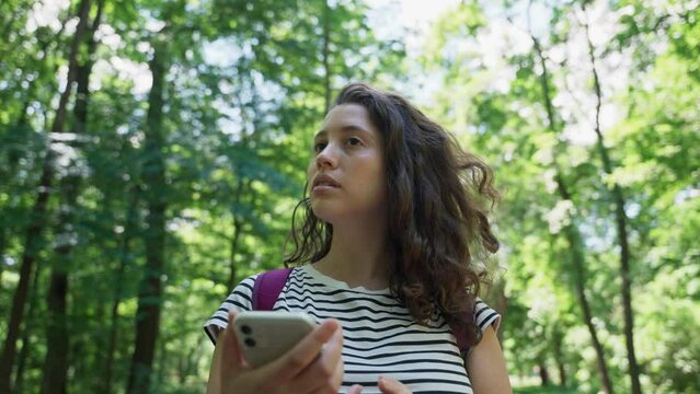 Female traveler in forest holds phone and looks for her location in map app. Stuck or lost young woman searches for signal or connection or whereabouts in digital map while hiking in wilderness