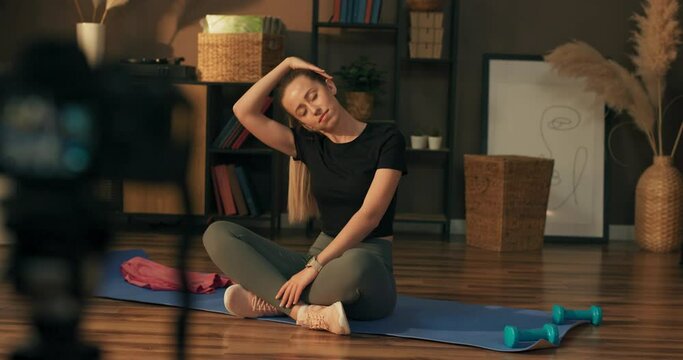Influencer does live for social network with trainings, meditation, yoga at home. The woman uses a camera and tripod to record the exercises. Sportswear ad.