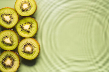 Kiwi slices lie on surface of rippled transparent fresh green water gel with fleck, waves, shadow, expanding circles
