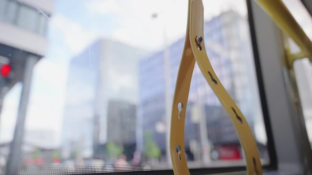 View from public bus window in Vienna, Austria as bus drives through the city. Handle straps for standing passengers to hold to during ride. City streets and bus seen through the windows