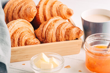 Fresh croissants, jam and coffee on white wooden table. Close up.