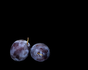 two ripe plums on a black background.