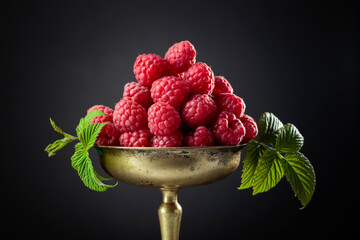 Fresh raspberries with leaves in an old brass dish.