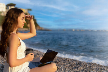 Teenage girl works on computer and talks on phone on the beach. concept of work and vacation together, digital nomads around the world