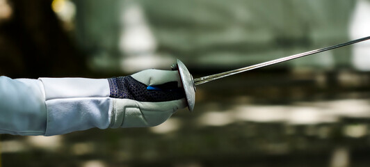 Epee of fencer with protected hand and arm against blurred background