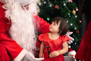 Fototapeta na wymiar Santa Claus talking to cute little child girl and she is looks Santa Claus by Christmas tree