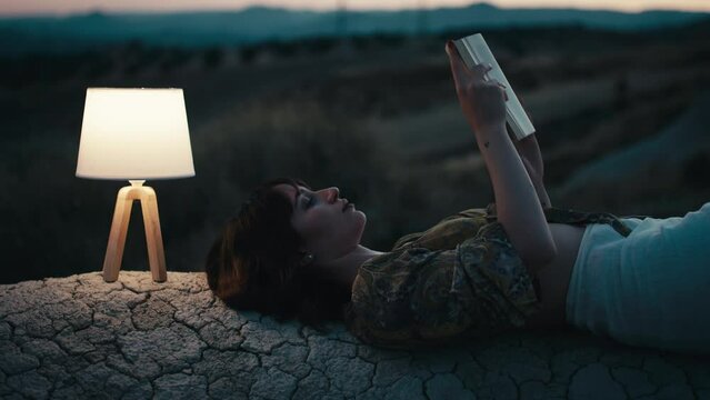 Woman reads a book in the evening on a rock with lamp