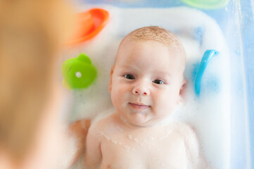 Baby bath time. Close-up detail view of mother bathing cute little peaceful baby in tub with water and bubbles lather.