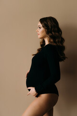 Beautiful young pregnant woman in underwear touching belly while posing on beige studio background